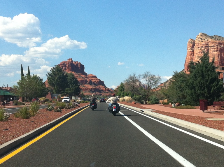 Sharing the road with motorcyclists, red sandstone formations on either side.